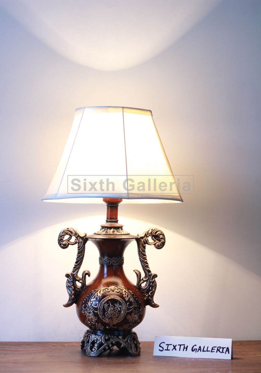 Antique floral table lamp with ornate bronze base and cream fabric shade lit on white wall background.