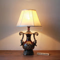 Antique floral table lamp with ornate metal base and cream fabric shade glowing warm light.