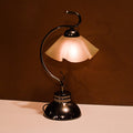 Black metal table lamp with curved arm and frosted glass scalloped shade, warm light illuminated.