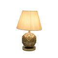 Table lamp with beige fabric shade and ornate spherical gold and bronze patterned base on round stand.