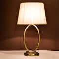 Pair of brass oval-frame table lamps with cream fabric shades on round bases.