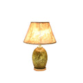 Table lamp with textured gold oval base and beige floral-patterned fabric shade on wooden platform.