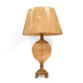 Golden antique table lamp with ornate base and beige fabric lampshade wrapped in plastic.