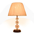 Table lamp with beige fabric shade and crystal spherical base on dark round platform.